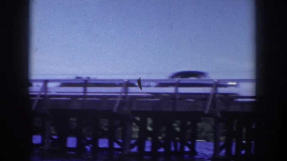 1953 Wisconsin home-movie view of a mid-century car moving across a metal bridge above the water.