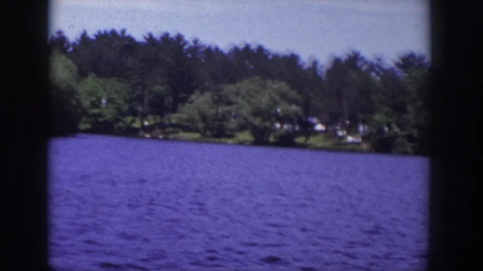 1953 Wisconsin 8mm lake view with blue water in the foreground and a wooded residential shoreline beyond.