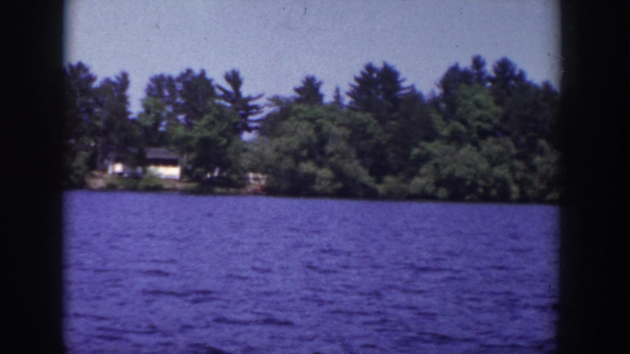 Lake water with a tree-lined shore and a distant light-colored house.