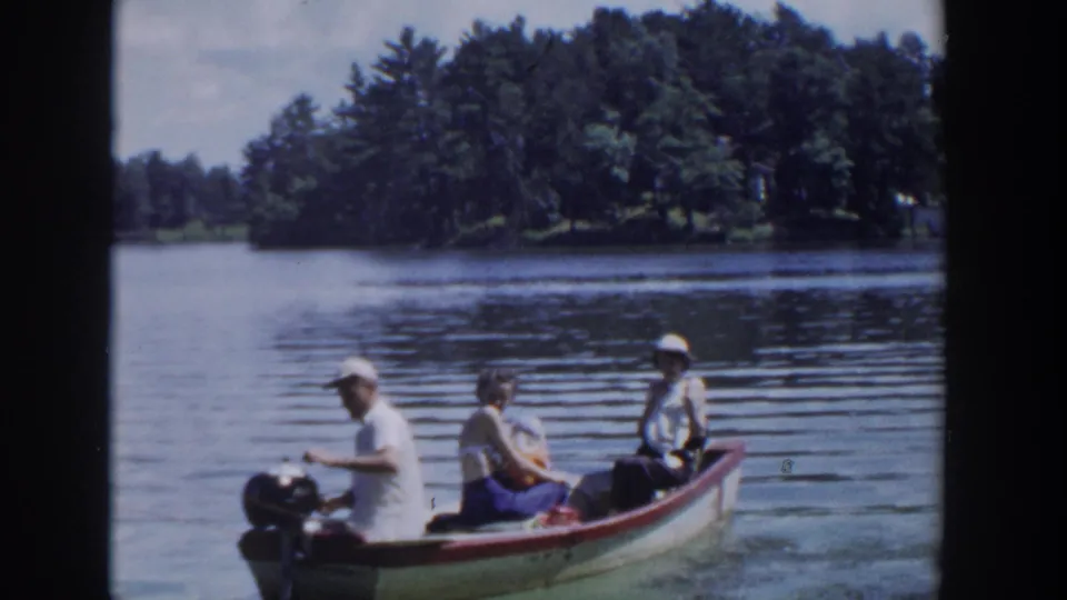 1953 Wisconsin lake scene with a man steering a small outboard motorboat while two adult passengers sit behind him.