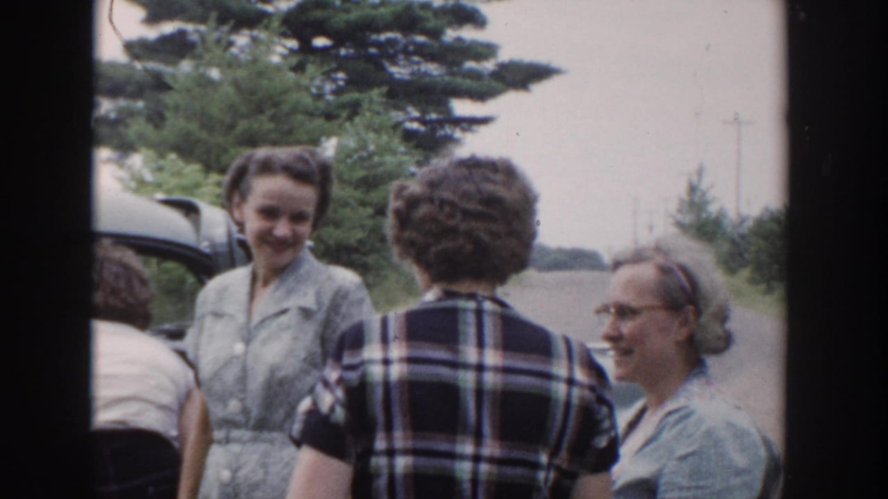 1953 Wisconsin home-movie frame showing women in mid-century clothing gathered beside a car on a rural roadside.