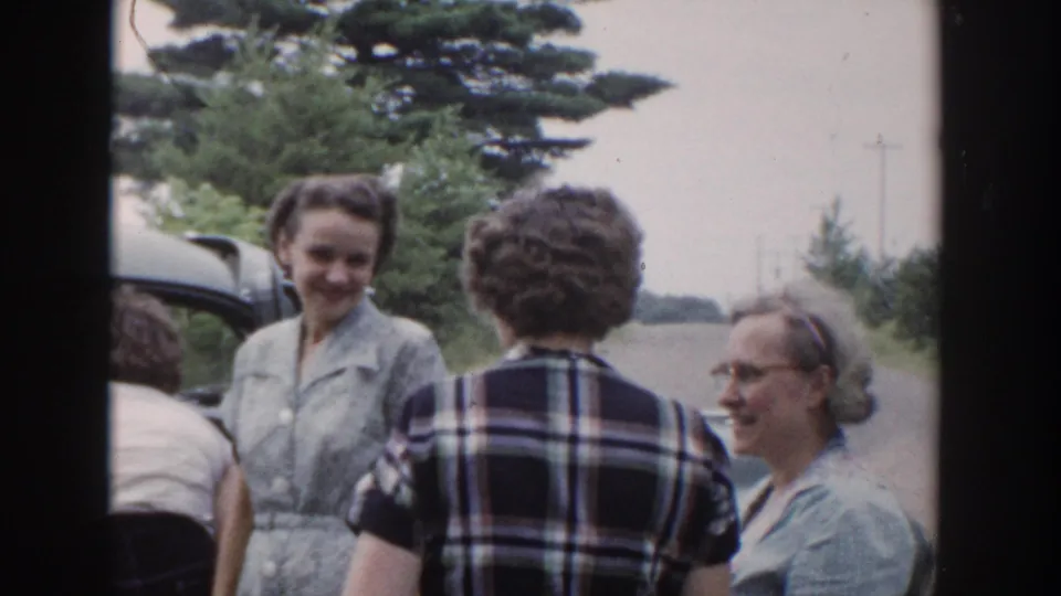 1953 Wisconsin home-movie frame showing women in mid-century clothing gathered beside a car on a rural roadside.