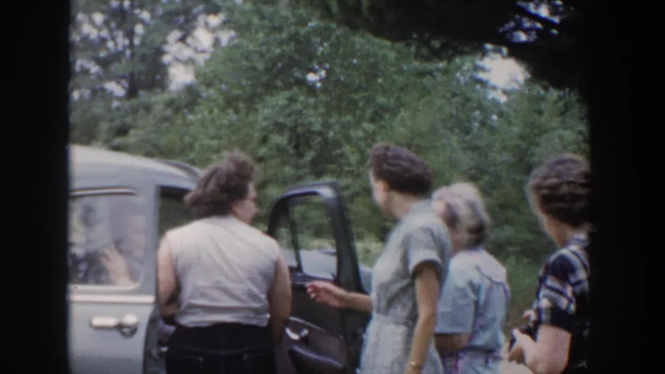 1953 Wisconsin roadside frame showing several women beside a light-colored car with its door open.