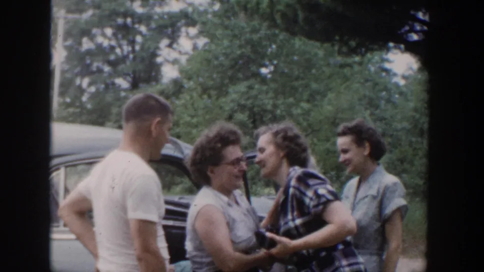 Adults in mid-century casual clothing smile and converse beside a car in Wisconsin home-movie footage dated 1953.