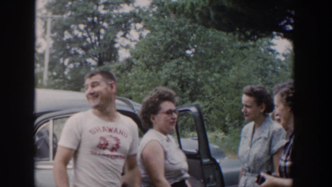 Man in printed T-shirt and women stand smiling beside an open car door.