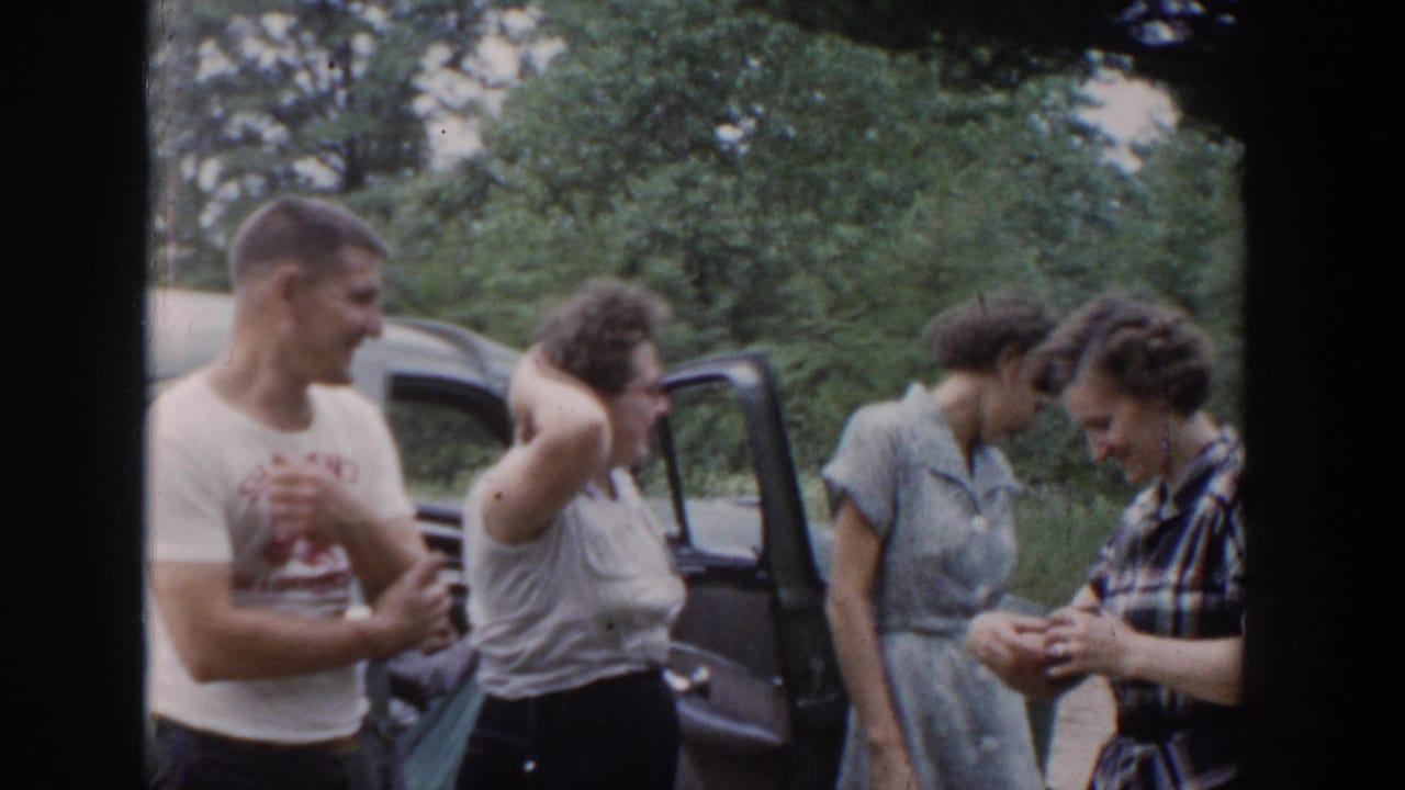 In 1953 Wisconsin home-movie footage, a man and three women gather beside an open car door in a wooded roadside setting.