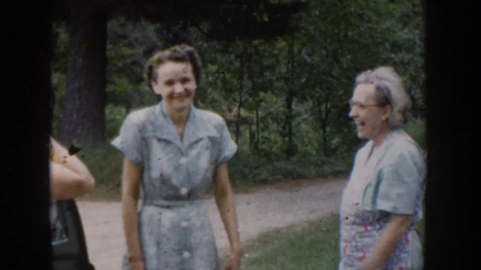 Two women in mid-century dresses smile in a wooded Wisconsin outdoor scene from the 1953 home movie.