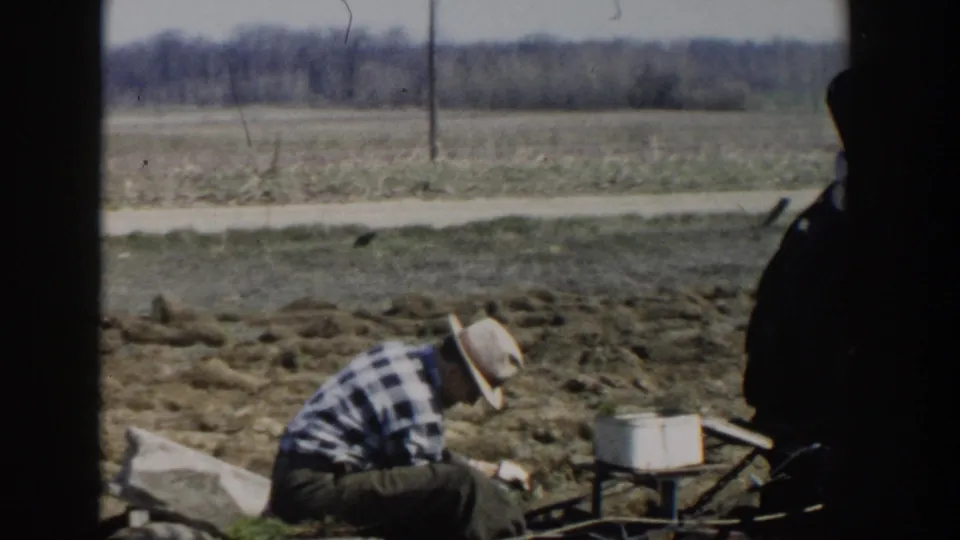 The final frame shows the Wisconsin Dells farm worker crouched beside a small implement and container, bordered by dark 8mm frame edges.
