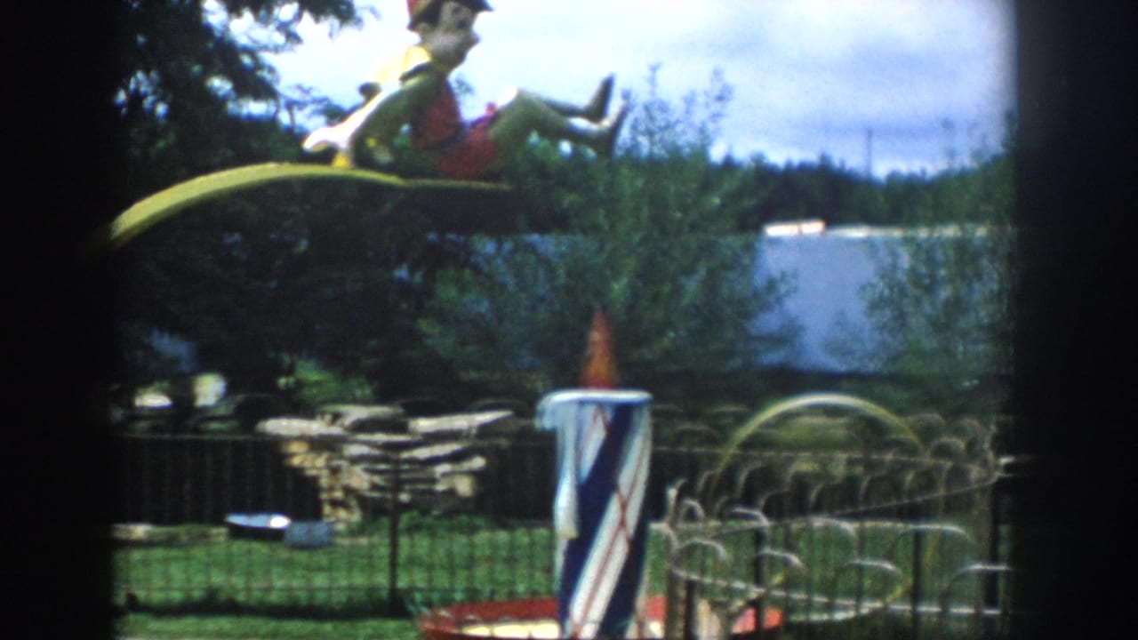Yellow arch with doll figure above a fenced deer area and striped pole.