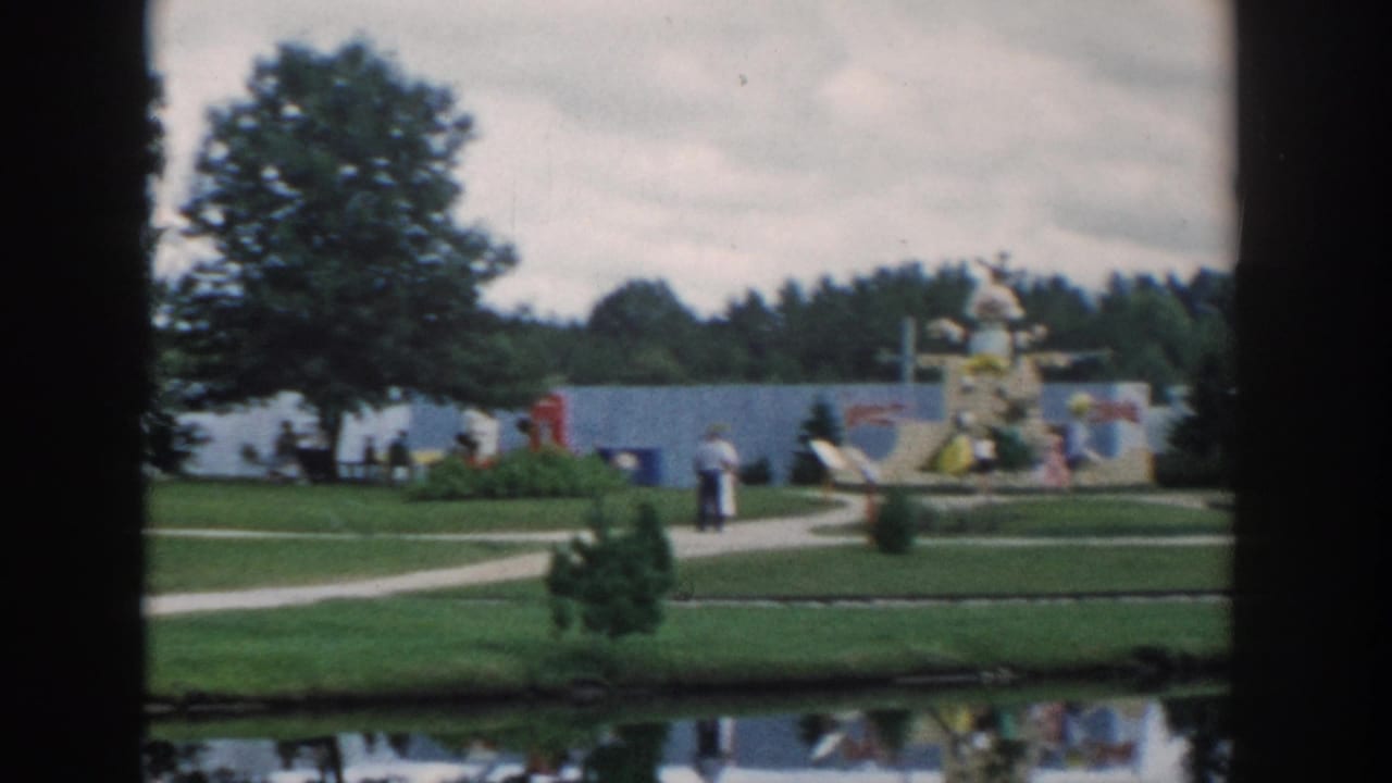 Visitors walk along paths near miniature displays, lawns, trees, and a pond.