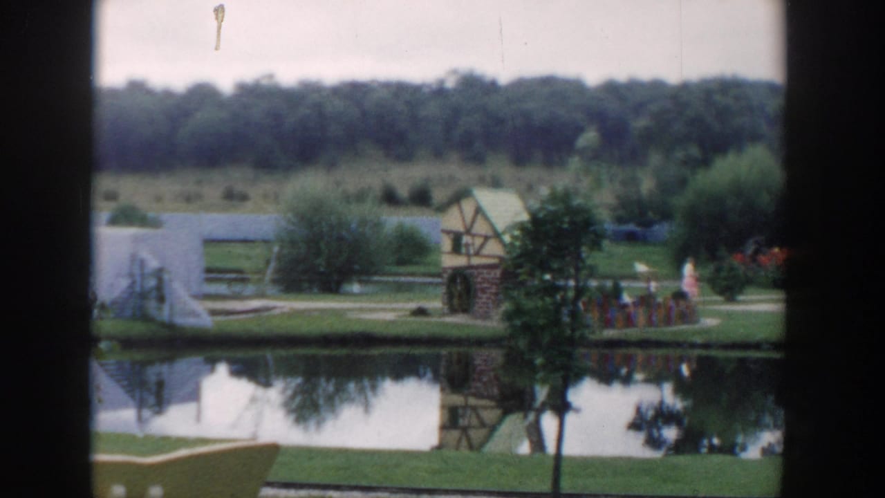 1954 Wisconsin Dells miniature-golf scene with a reflective pond, decorative mill, landscaped paths, and small distant figures.