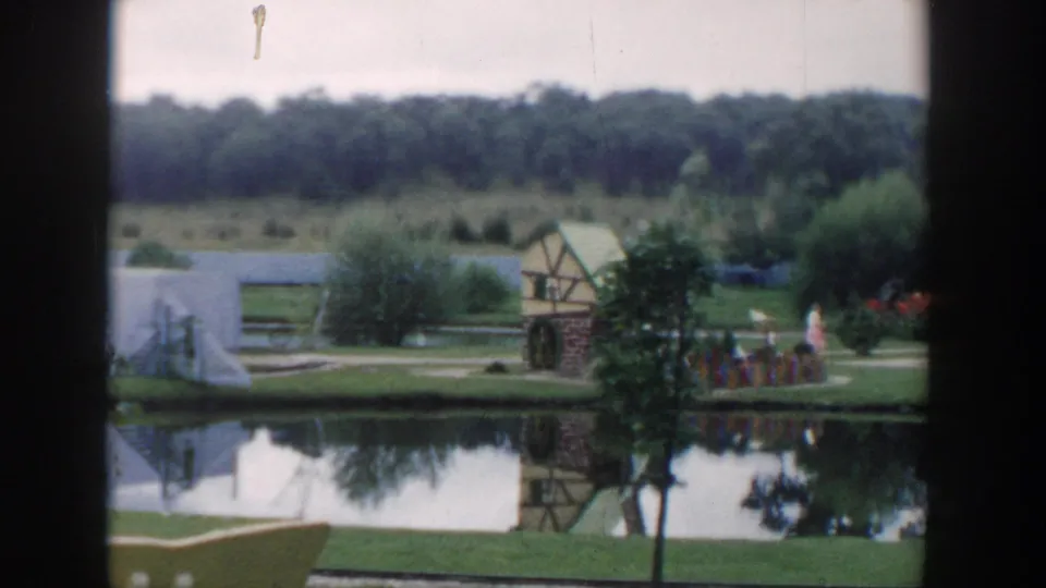 1954 Wisconsin Dells miniature-golf scene with a reflective pond, decorative mill, landscaped paths, and small distant figures.