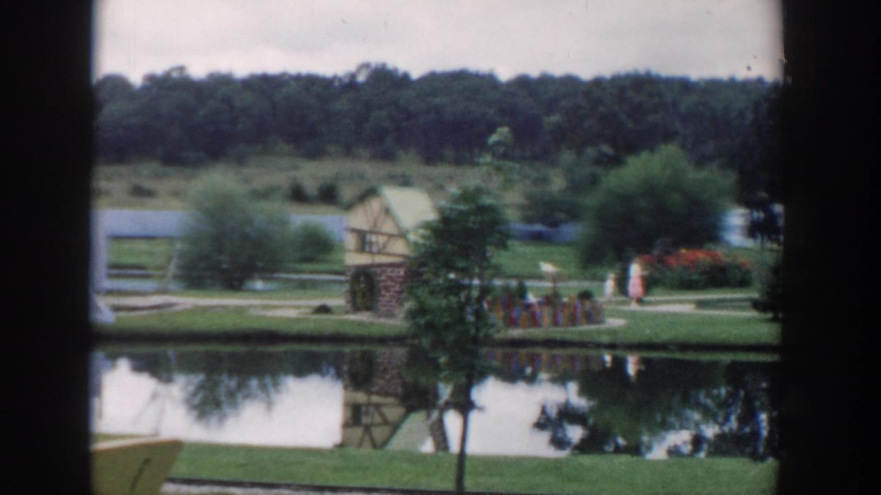 Pond and miniature-golf landscape with mill building, trees, paths, and visitors in the distance.