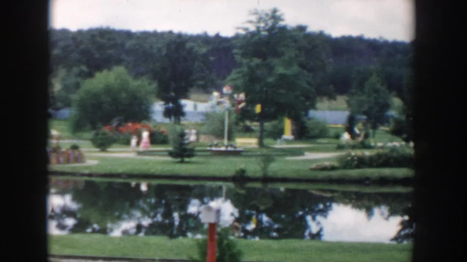A 1954 Wisconsin Dells miniature-golf view shows landscaped lawns, a pond, planted beds, and visitors across the grounds.