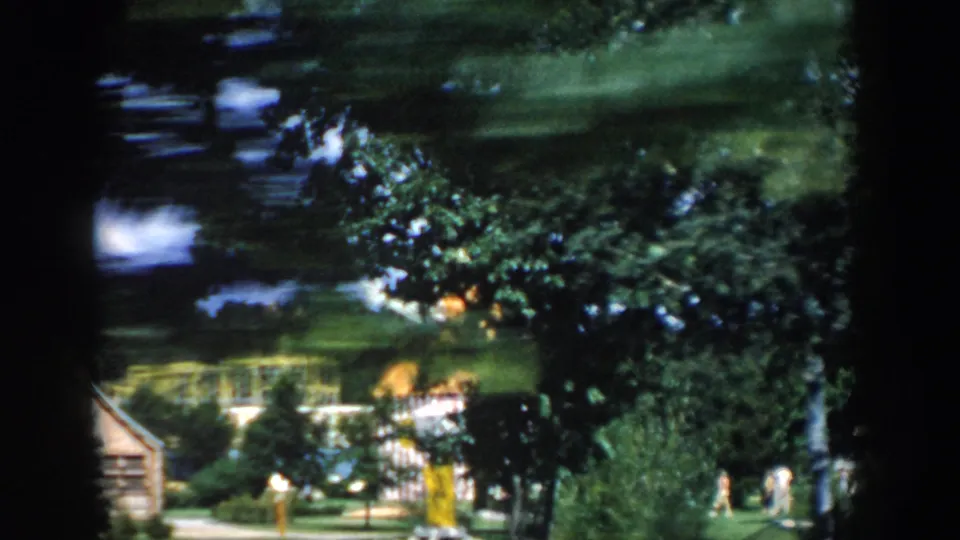 Motion-blurred 1954 Wisconsin Dells 8mm frame with reflected trees, green lawn, and yellow park fixtures passing the camera.