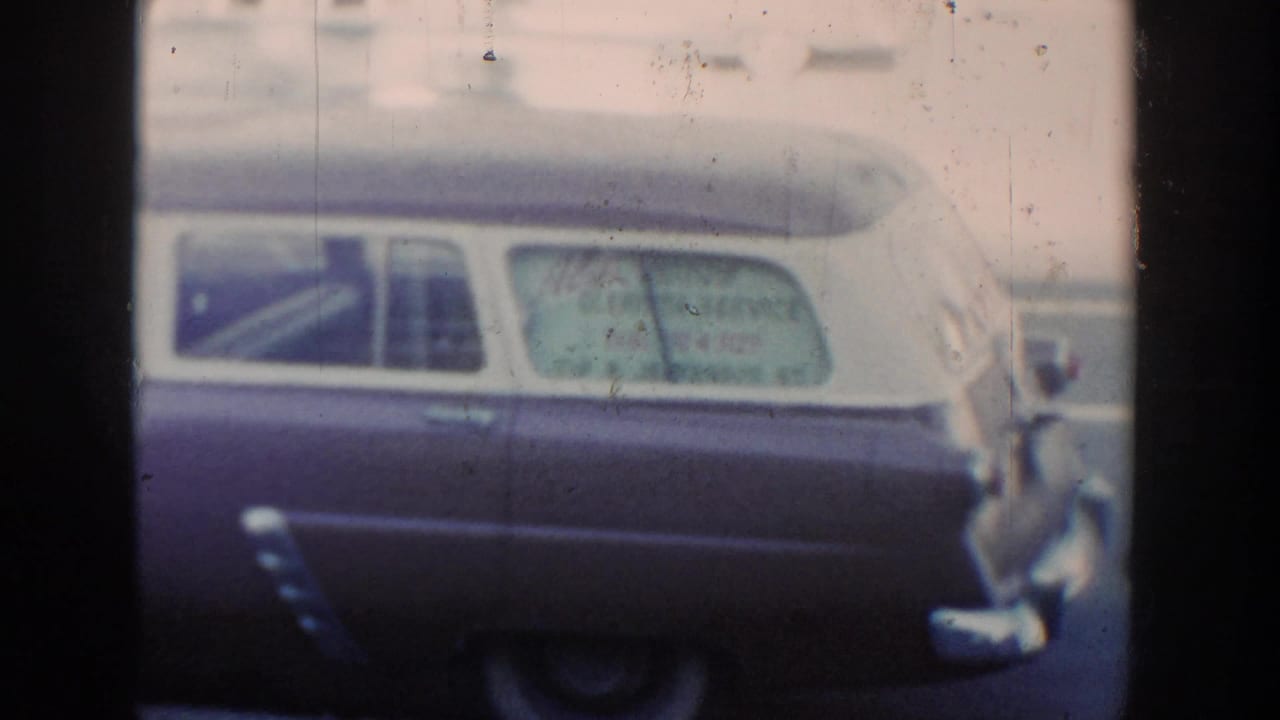 1954 Wisconsin Dells home-movie frame showing a dark and light two-tone station wagon with service lettering on the rear side window.