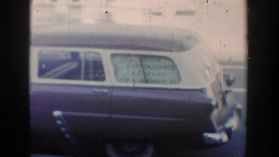 1954 Wisconsin Dells home-movie frame showing a dark and light two-tone station wagon with service lettering on the rear side window.