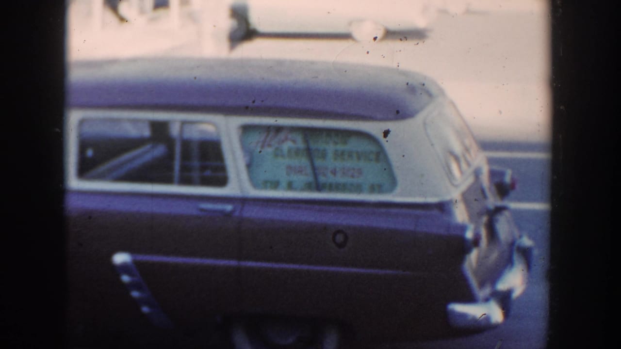 Side view of a two-tone station wagon with hand-lettered service text in the rear window.