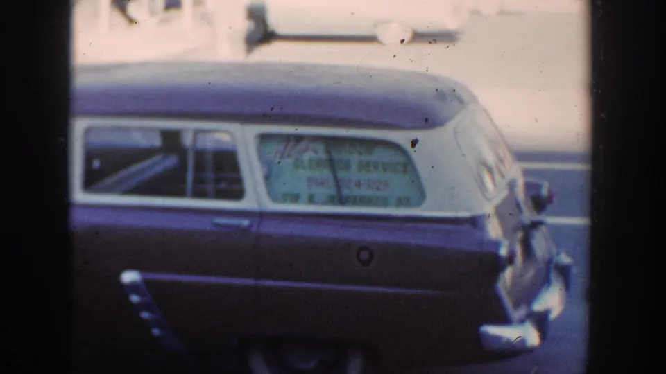 Side view of a mid-century two-tone station wagon in the 1954 Wisconsin Dells footage, with business text visible on the rear glass.