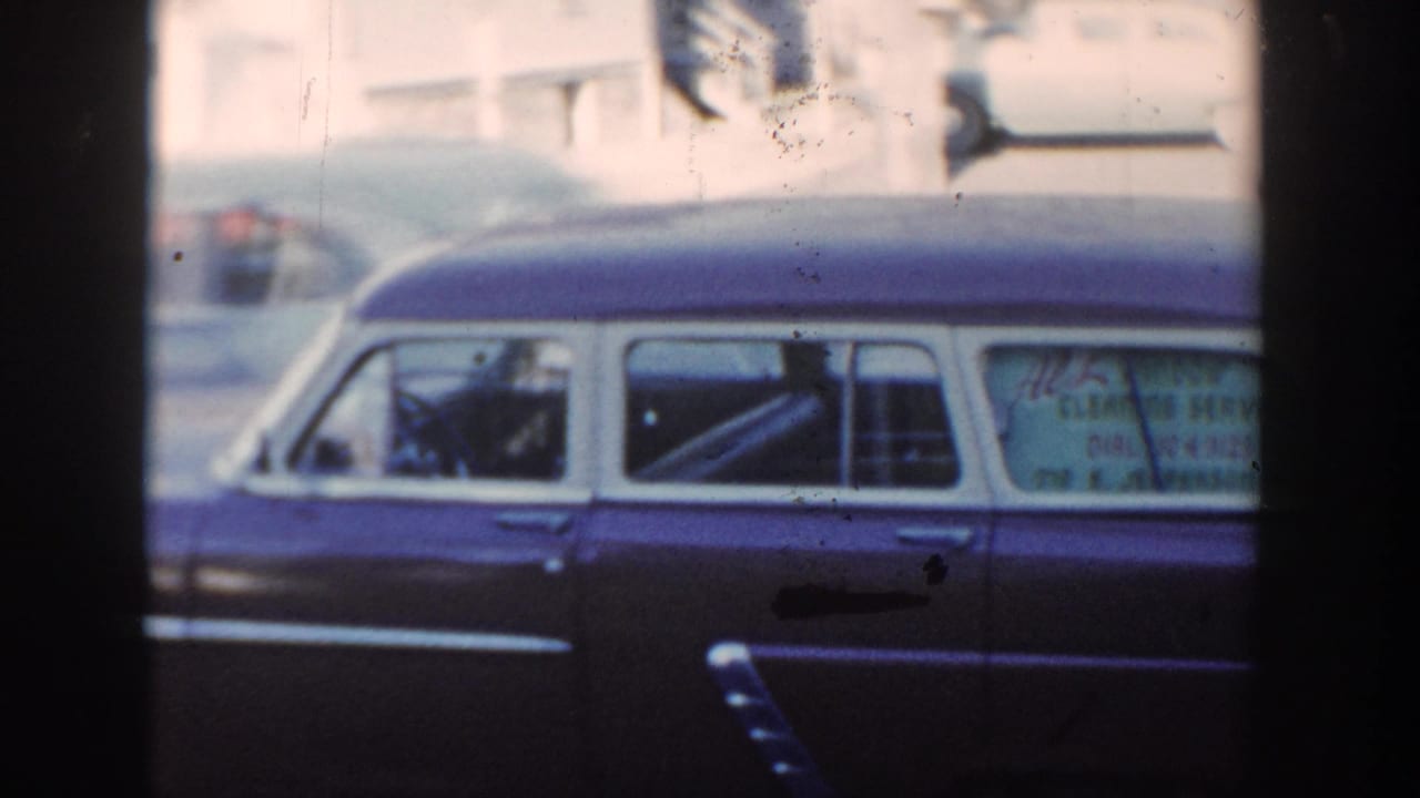 1954 Wisconsin Dells home-movie frame showing a dark station wagon with white roof and rear-window service lettering on a street.