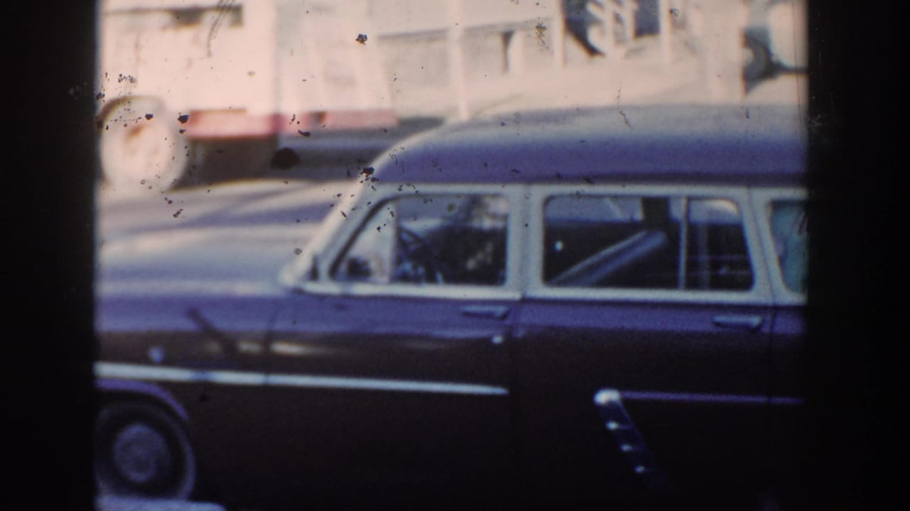Dark station wagon parked beside a street with another vehicle passing in the background.