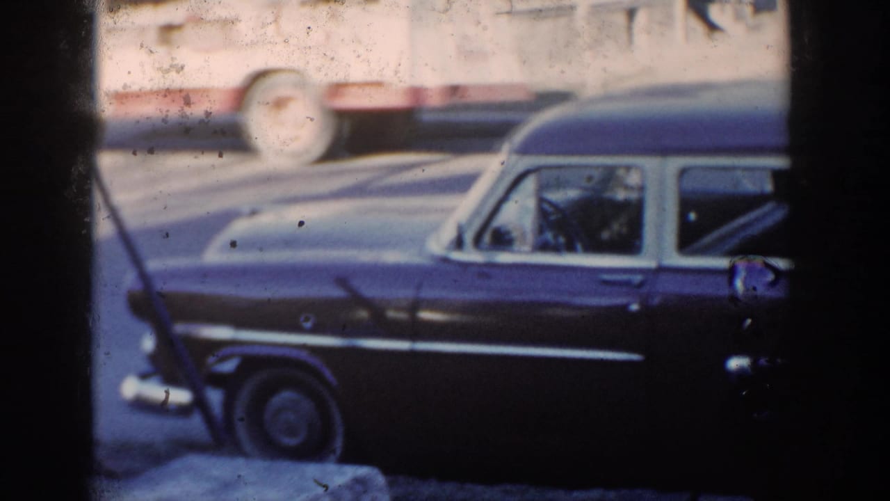 1954 Wisconsin Dells home-movie frame showing the station wagon front and a partially visible adult figure near the curb.