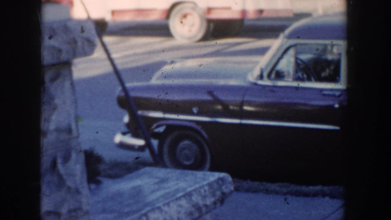 1954 Wisconsin Dells frame showing a dark station wagon and a partially visible adult figure standing near the front fender.