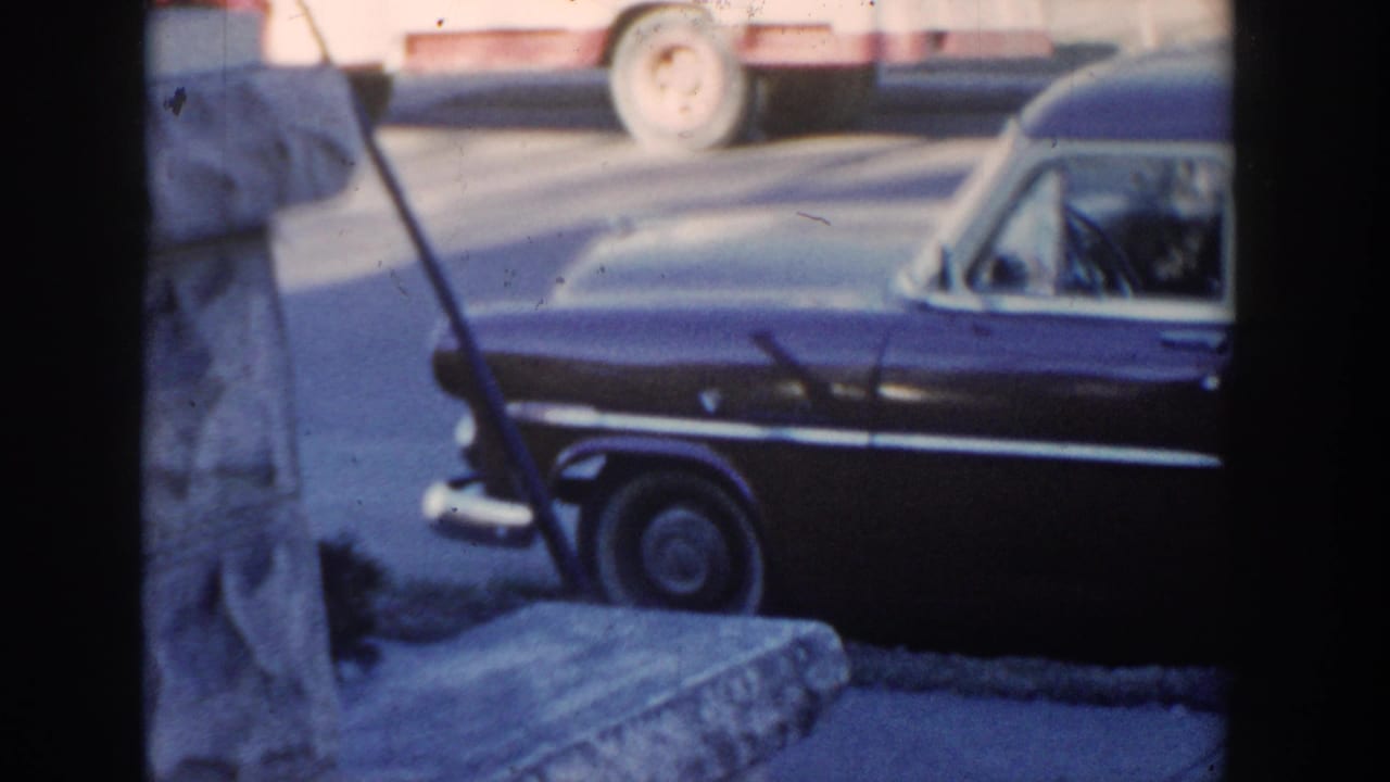 1954 Wisconsin Dells roadside view of a dark two-tone wagon or hearse-like car with chrome trim and a cropped person at the frame edge.