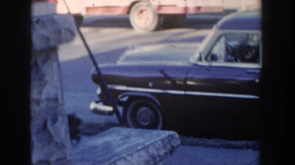 1954 Wisconsin Dells roadside view of a dark two-tone wagon or hearse-like car with chrome trim and a cropped person at the frame edge.