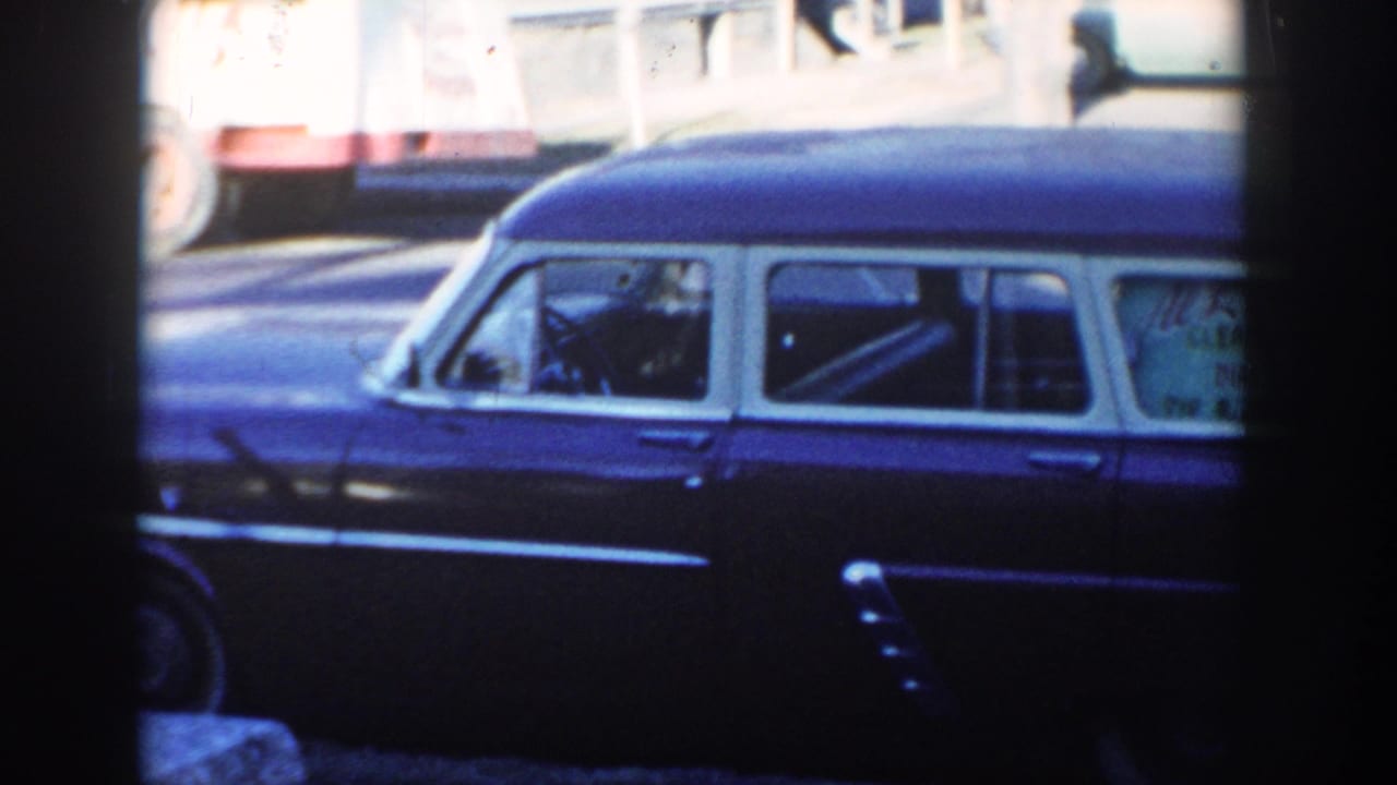 1954 Wisconsin Dells home-movie frame showing a dark blue station wagon with chrome trim viewed through porch or wall posts.