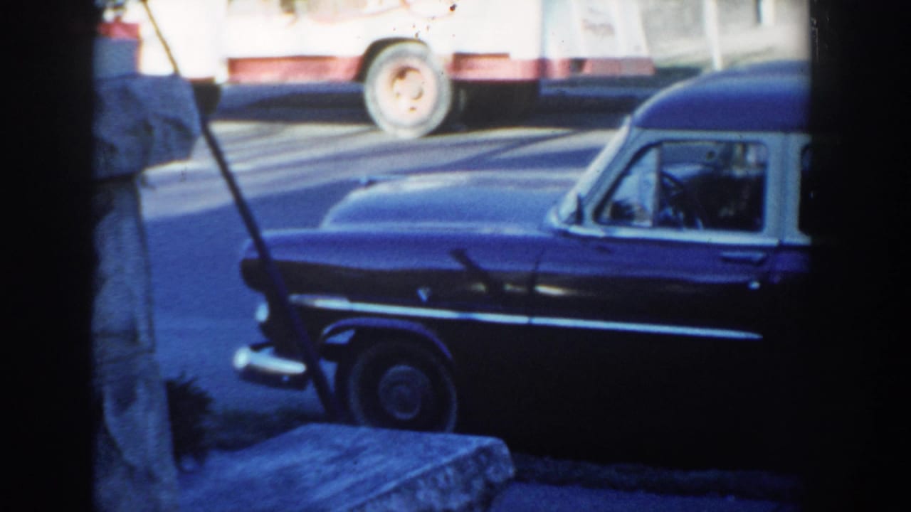 1954 Wisconsin Dells frame showing the front of a dark blue station wagon, whitewall tire, stone wall, and passing truck.