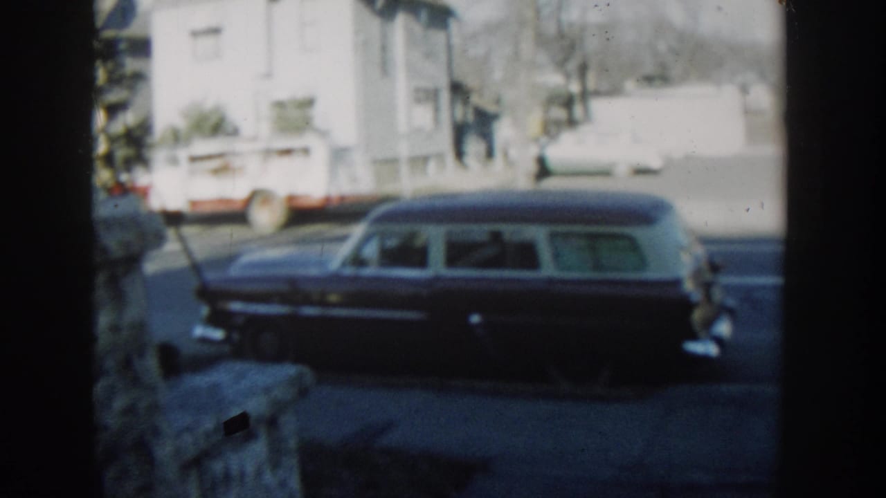 Parked station wagon on a residential street with a white house behind it.