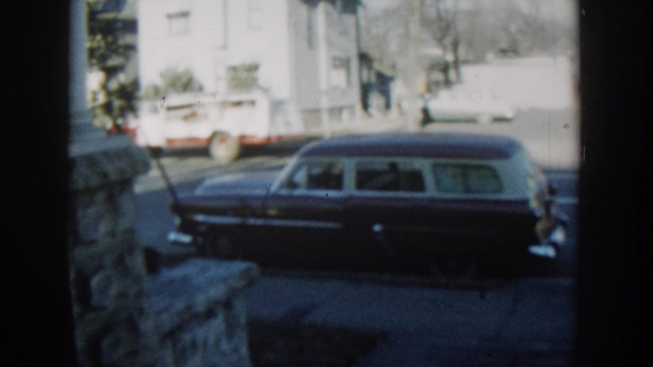 The station wagon is seen again from the porch area, with chrome details, a white house, and a utility truck visible across the street.
