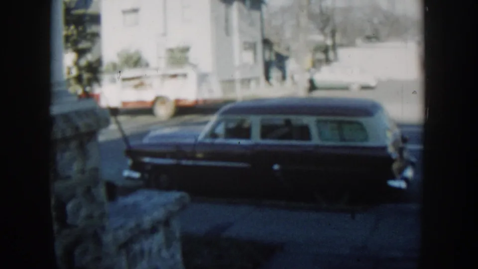 The station wagon is seen again from the porch area, with chrome details, a white house, and a utility truck visible across the street.