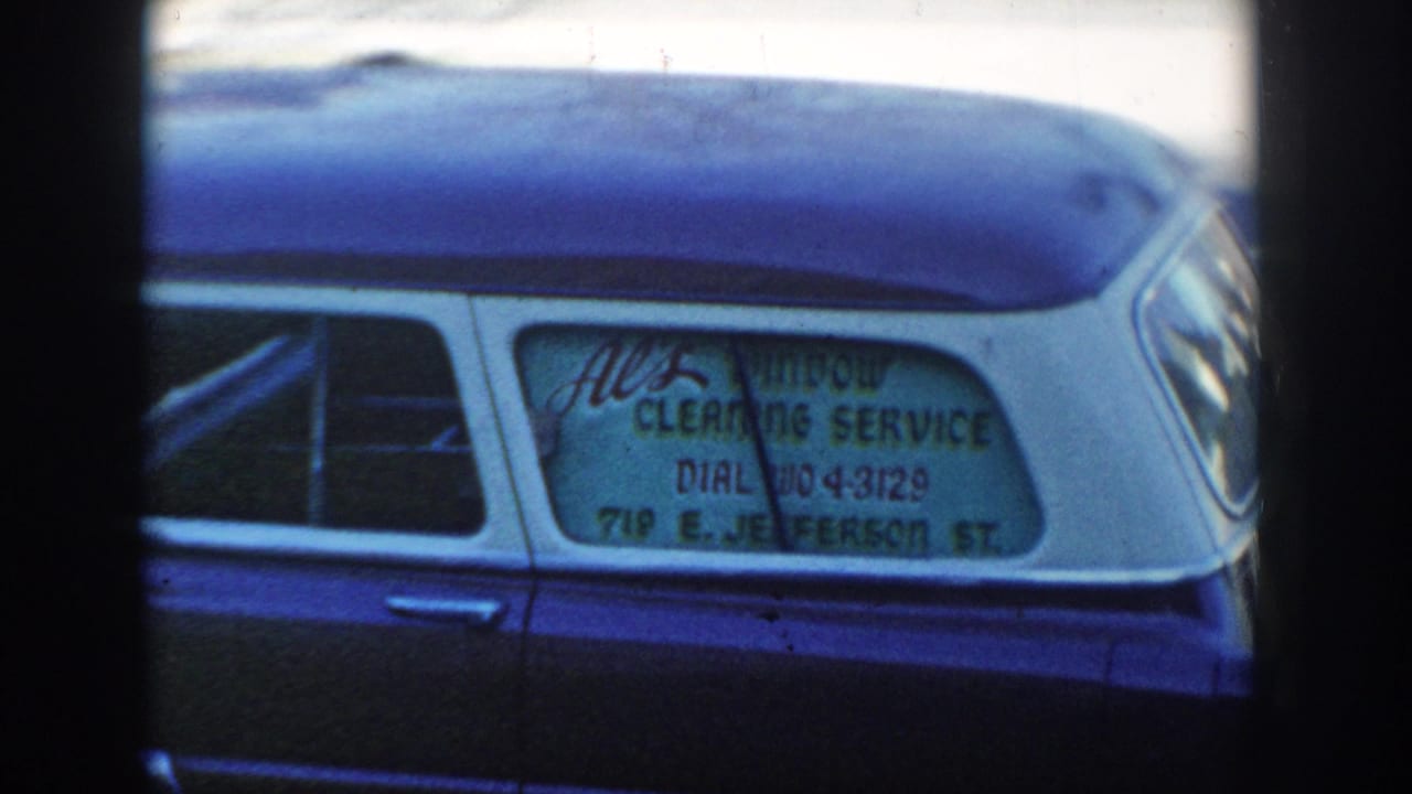 Blue station wagon rear side window with hand-painted window cleaning service sign.