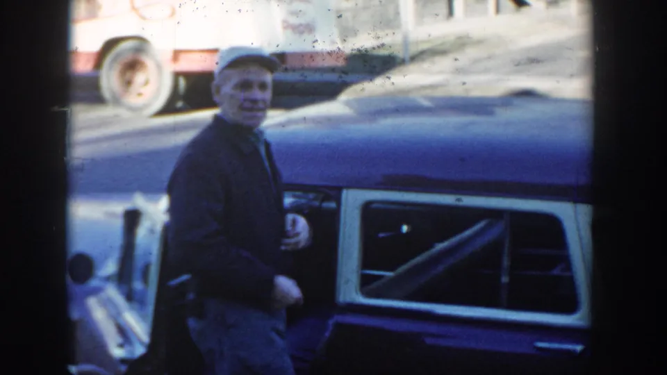 1954 Wisconsin Dells frame showing an adult man in a cap beside the blue station wagon with the service sign partly visible.