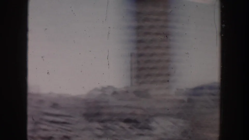 1956 Grand Rapids car-window view of a construction area with stacked masonry or beams and a tall soft-focused structure beyond.