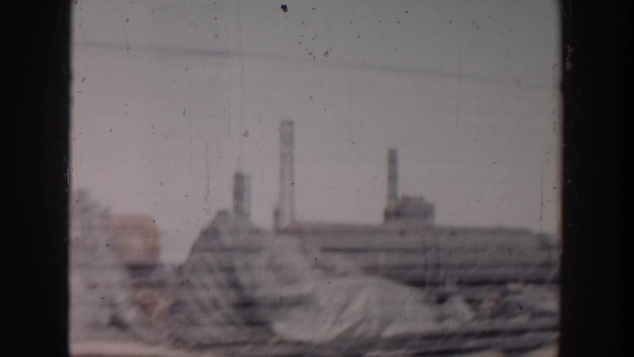 Industrial construction area with piles of material and chimney-like stacks in the distance.