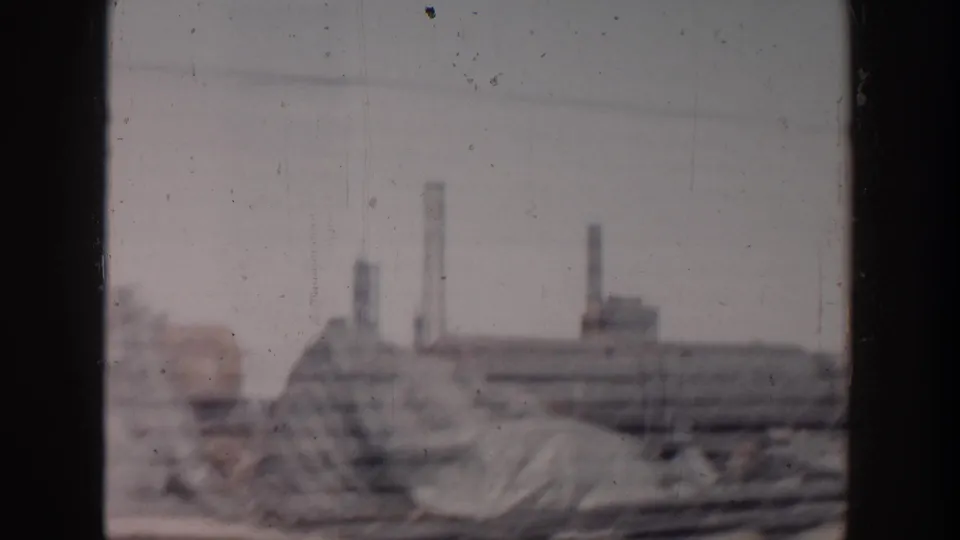 Grand Rapids construction site view with earth or masonry piles, low industrial forms, and distant chimney stacks in soft 8mm focus.