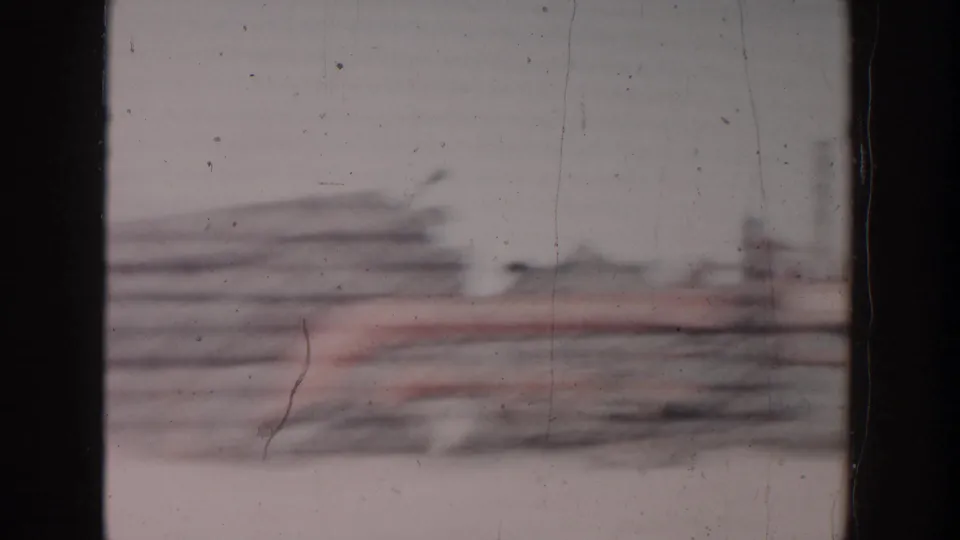 1956 home-movie frame showing stacked beams or masonry at a Grand Rapids construction site, partly obscured by motion blur and film wear.