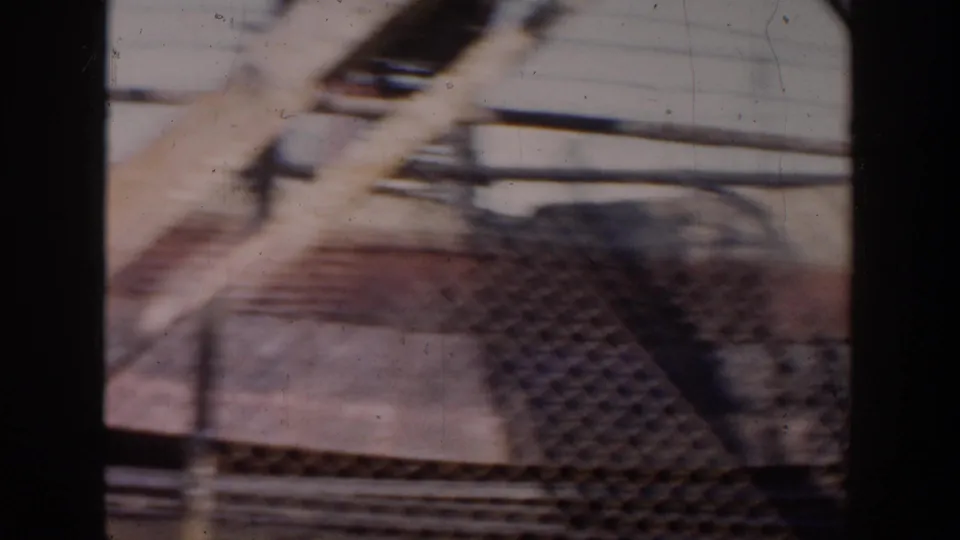 A red dump truck passes near a worksite barrier, seen with motion blur from the 1956 Grand Rapids home movie.