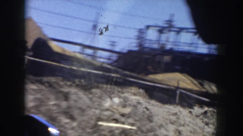 1956 Grand Rapids home-movie frame showing a moving-car view of dirt grading, utility lines, and construction material through a window.