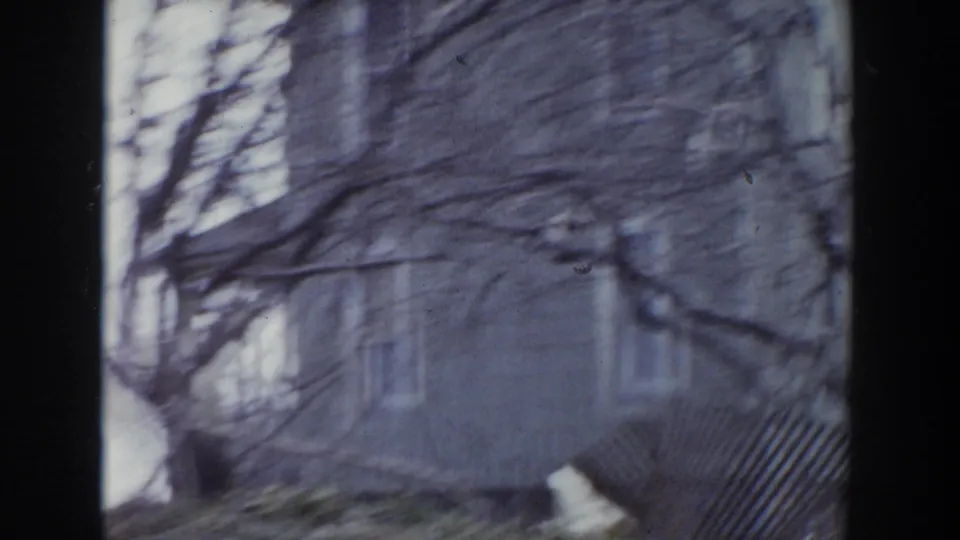 Handheld 8mm view in Grand Rapids showing a building exterior, bare branches, and fence seen through a window.