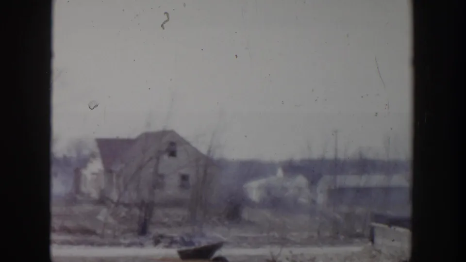 Faded 1956 Grand Rapids view of a distant house, bare trees, and low neighborhood horizon from behind a window.