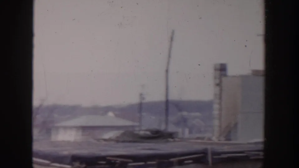 1956 Grand Rapids home-movie frame showing a soft rooftop view with utility poles, pale structures, and distant low buildings.