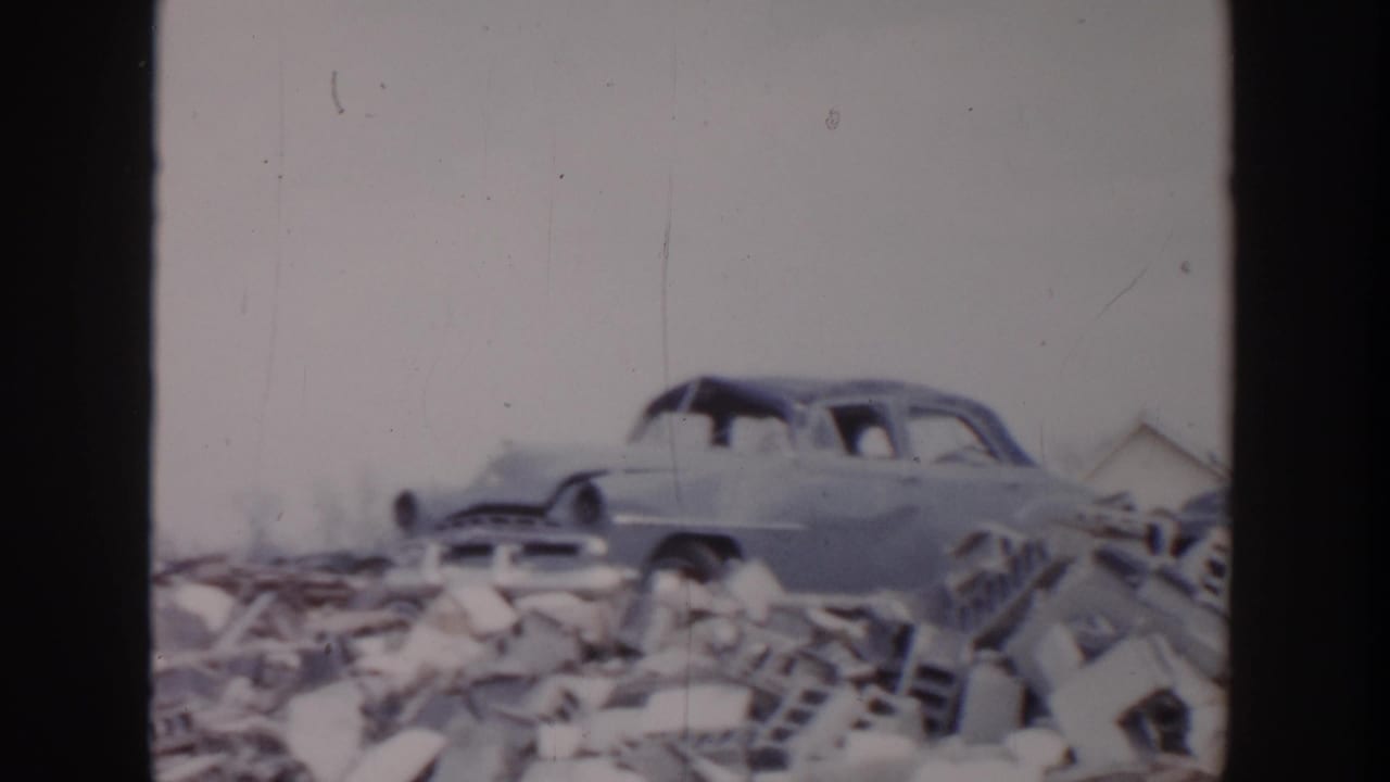 Pale 1950s sedan beside a pile of broken bricks and debris.