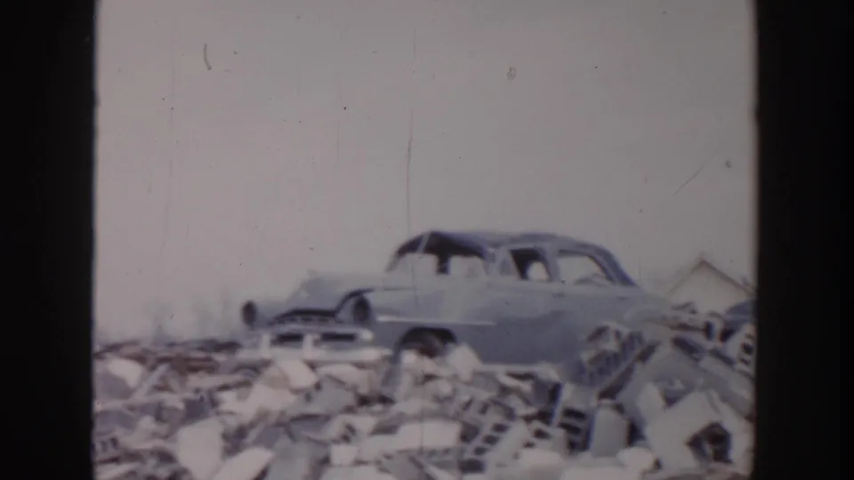 1956 Grand Rapids tornado aftermath with a rounded sedan partly obscured by rubble and scattered building debris.