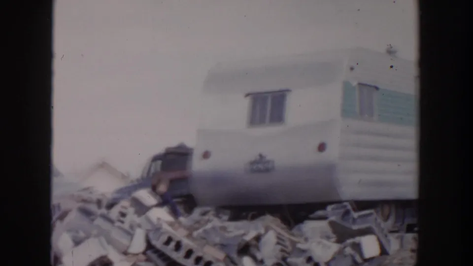 The 8mm frame shows a white travel trailer beside storm rubble and a partially visible vehicle in Grand Rapids.