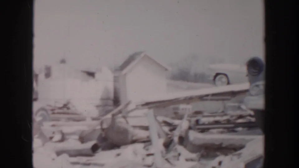 1956 Grand Rapids marina aftermath with snow, damaged dock material, a small shed, and a partly obscured 1950s automobile.
