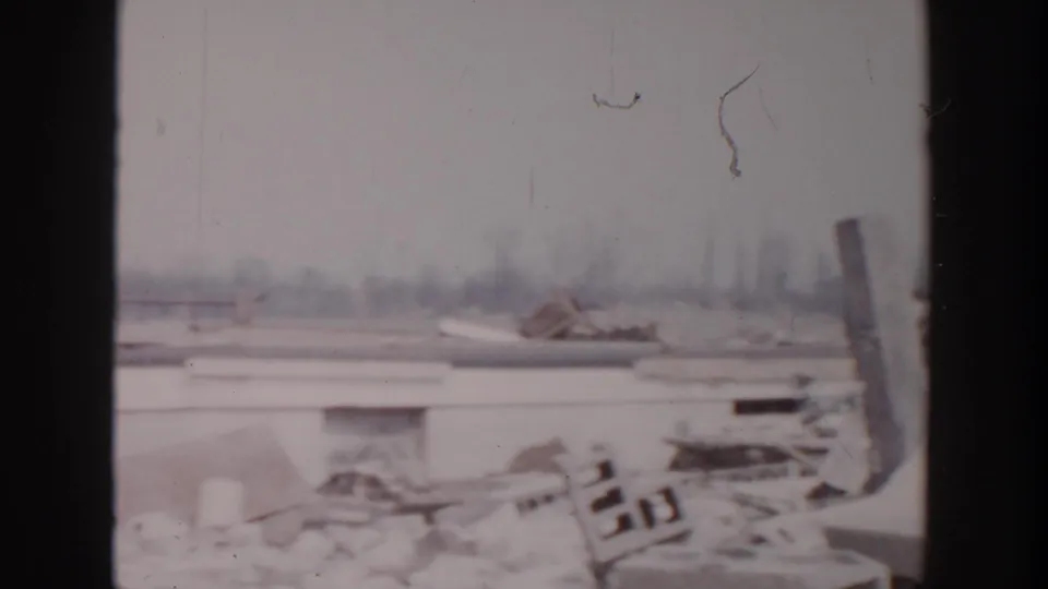 1956 Grand Rapids marina view with snow-covered dock wreckage, scattered boards, frozen water, and a blurred winter shoreline.